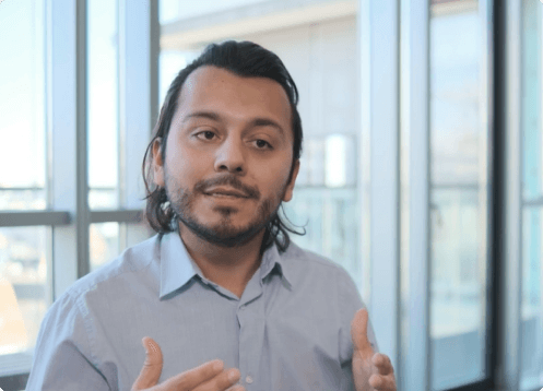 Man speaking with glass windows in background.