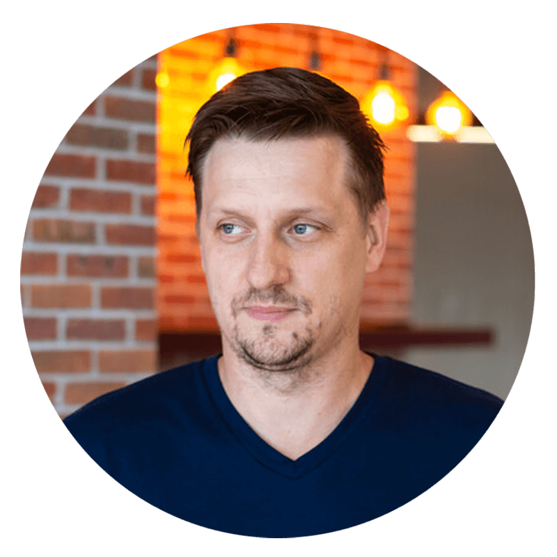 Man with dark hair, blue shirt, brick background.