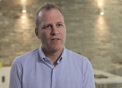 Man in a blue shirt speaking indoors.