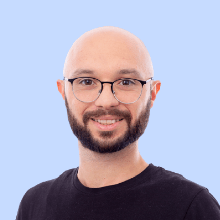 Bald man with glasses smiling against light blue background.