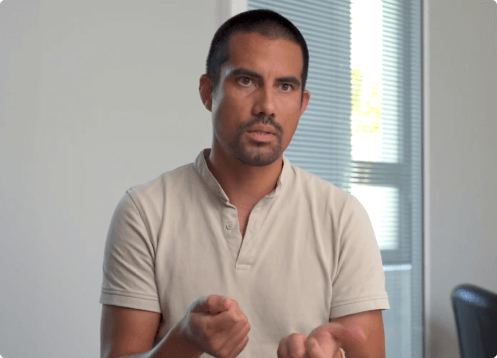 Man speaking, gesturing with hands in an office setting.