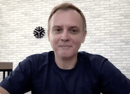 Man sitting, smiling, brick wall background.