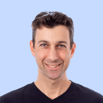Man smiling, wearing a black shirt, light blue background.