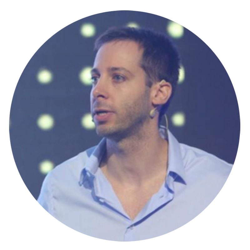 Man wearing a light blue shirt, talking on stage.